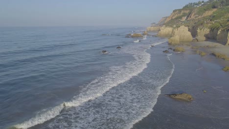 Aerial-shots-of-El-Matador-beach-over-breaking-waves-and-rocks-on-a-hazy-summer-morning-in-Malibu,-California