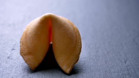 un primer plano dando vueltas alrededor de una galleta de la fortuna girando lentamente sobre el fondo de la mesa gris.