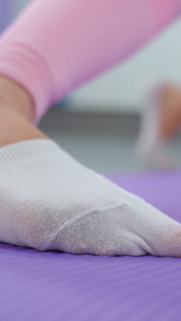 primer plano del pie en calcetines deportivos blancos en una alfombra de ejercicio púrpura, estirándose durante la sesión de entrenamiento, la otra pierna arrodillada en la alfombra aparece ligeramente borrosa en el fondo