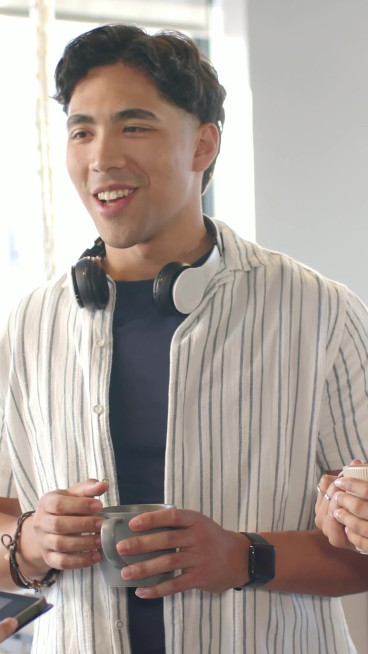 Video verticale: Uomo che ascolta con tazza e cuffie nella sala relax, risponde ai gesti del team.