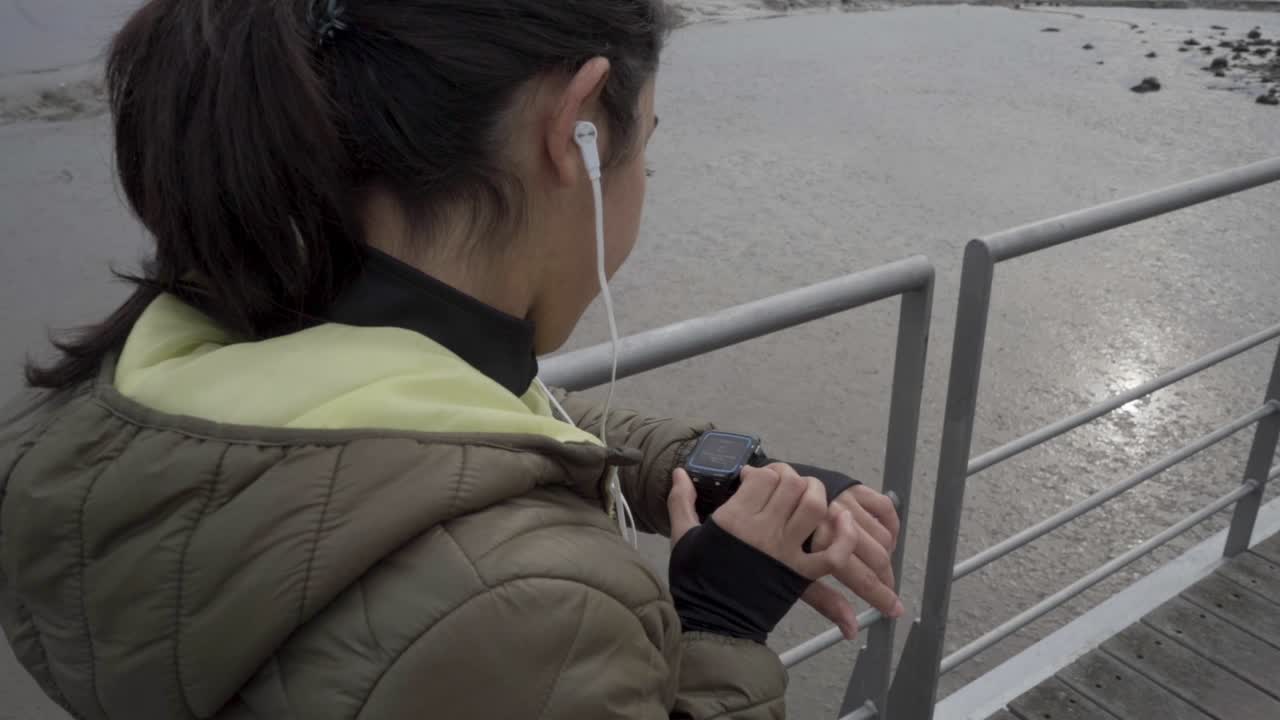 mujer joven morena poniendo reloj deportivo en el muelle de madera