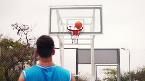 Vista-Posterior-De-Un-Jugador-Irreconocible-Lanzando-Una-Pelota-En-Un-Aro-De-Baloncesto,-La-Pelota-Golpea-El-Aro-Y-Anota.-Tiro-En-Cámara-Lenta