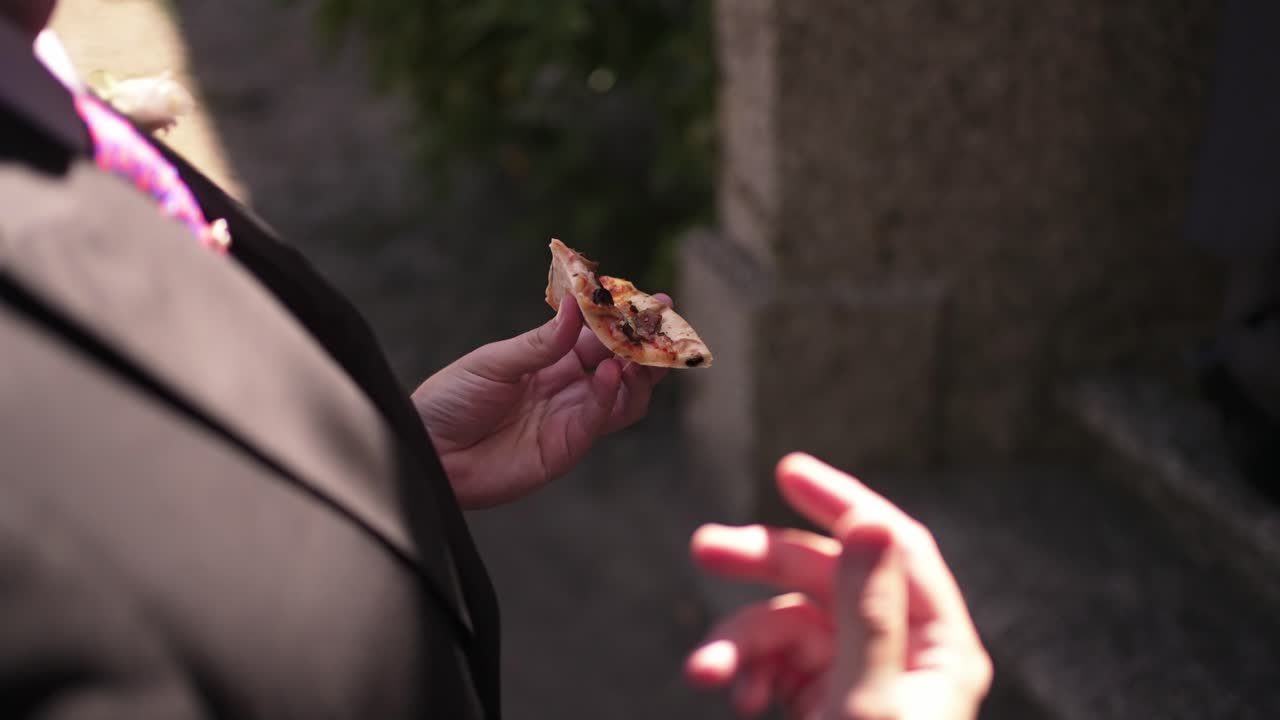 Person in a suit holding a slice of pizza outdoors