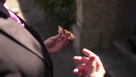 person in a suit holding a slice of pizza outdoors