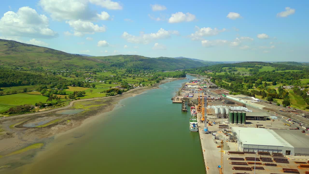 Wide, advancing aerial video of the Newry River and surrounding industry in Warrenpoint, County Down, Northern Ireland, UK on a bright and sunny day. Filmed in 4K, 60FPS and with Rec709 color.