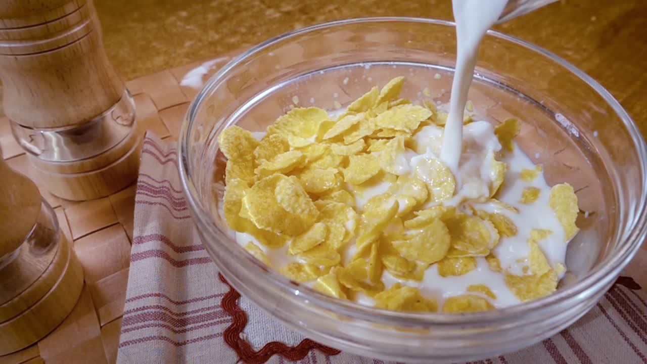 Knusprige gelbe Cornflakes in die Schale für ein köstliches Frühstück mit Milch am Morgen. Zeitlupe mit rotierender Kamerafahrt