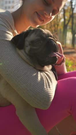 girl cuddling a pug puppy in a park