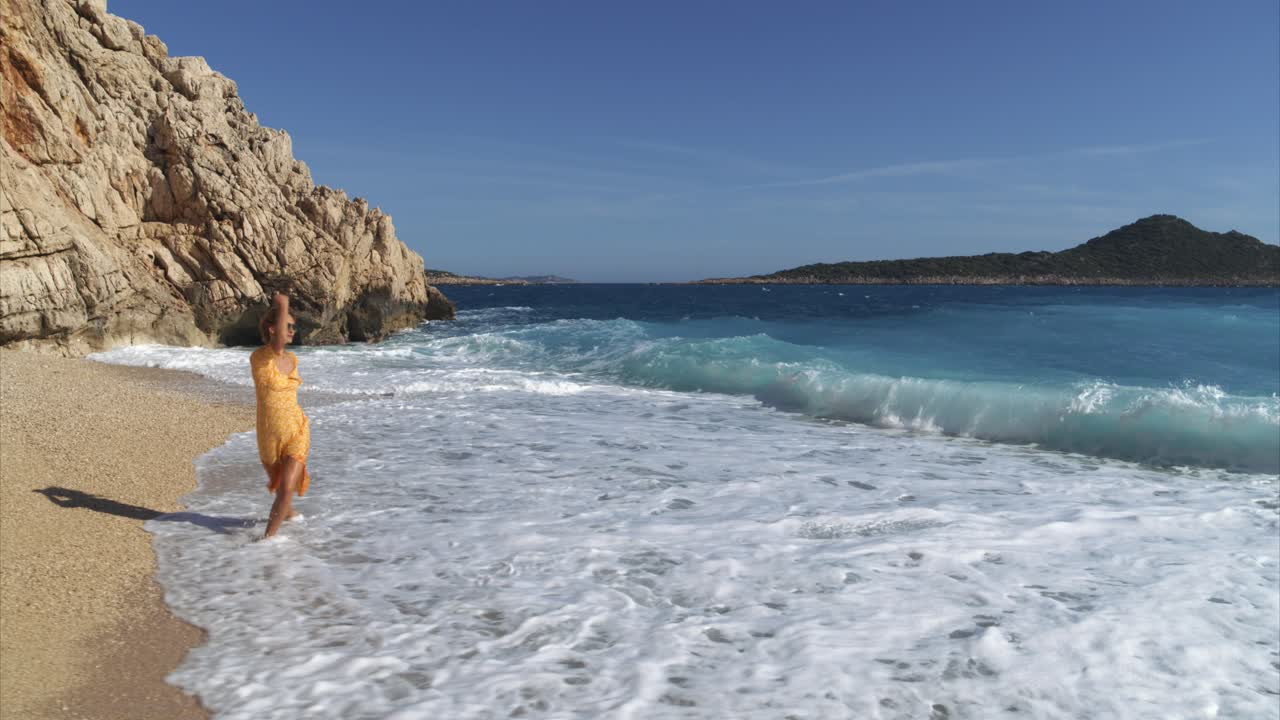 mulher modelo com vestido amarelo caminha pelas águas na praia