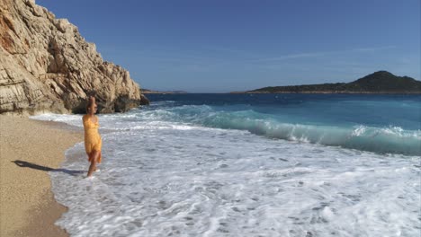 mujer modelo con vestido amarillo camina por las aguas de la playa