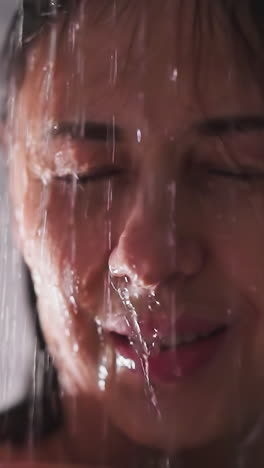 smiling woman under pouring water in shower closeup. relaxed lady enjoys spa procedures standing in bathroom. recreation and hygienic routine