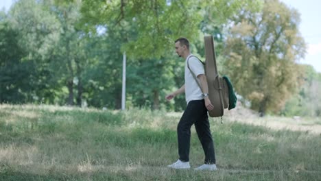 joven caminando con la guitarra en la calle cerca del bosque