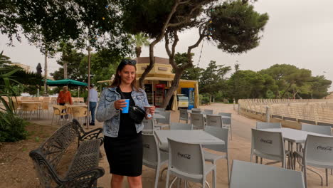 shot of young girl bringing drinks on a table in an outdoor café beside a popular tourist spot in malta on a cloudy day