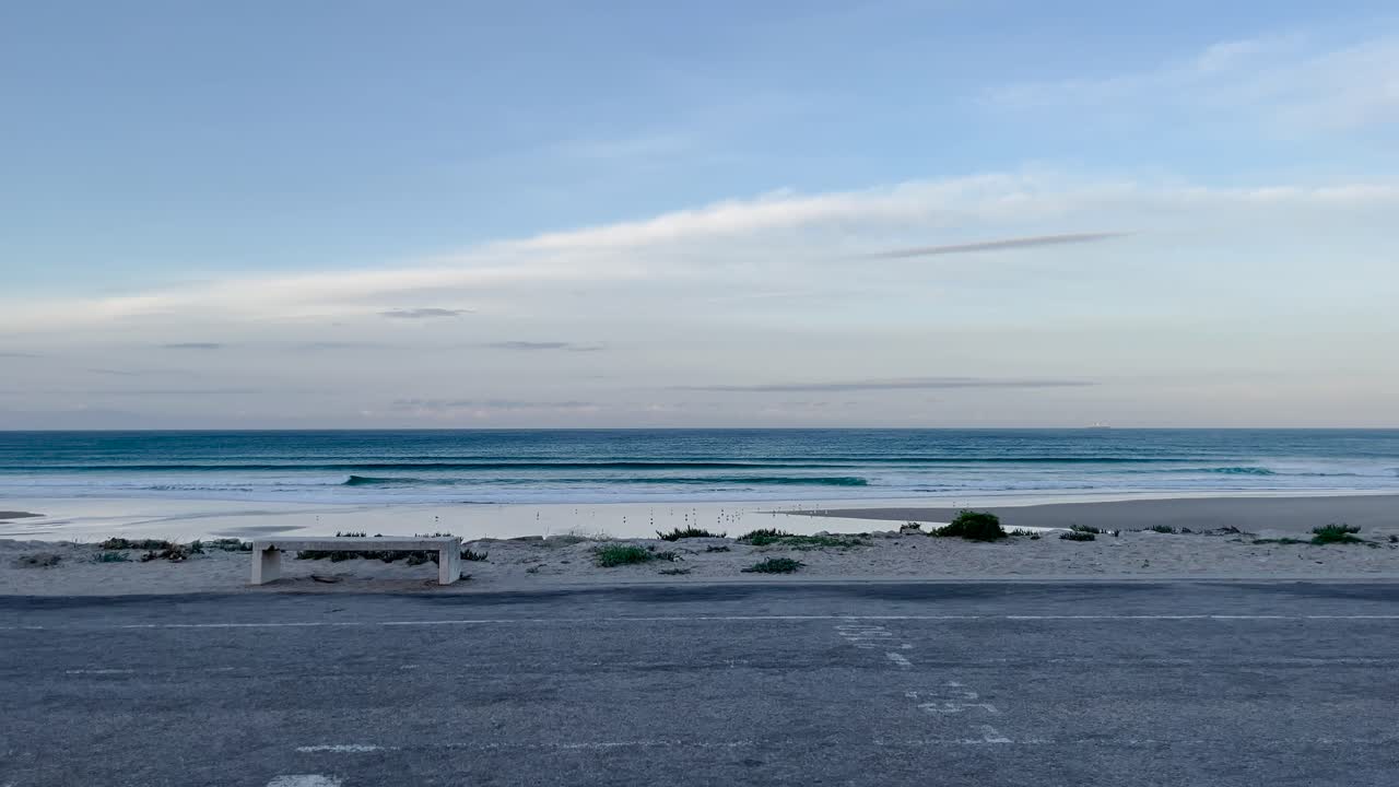 Early morning calm beach with gentle waves under soft pastel blue sky and distant coastline