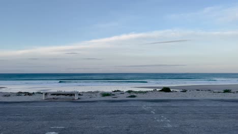 early morning calm beach with gentle waves under soft pastel blue sky and distant coastline