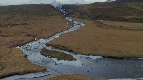 curve river running down the fields by svodufoss waterfall with glacier-capped stratovolcano of snaefellsjokull in background