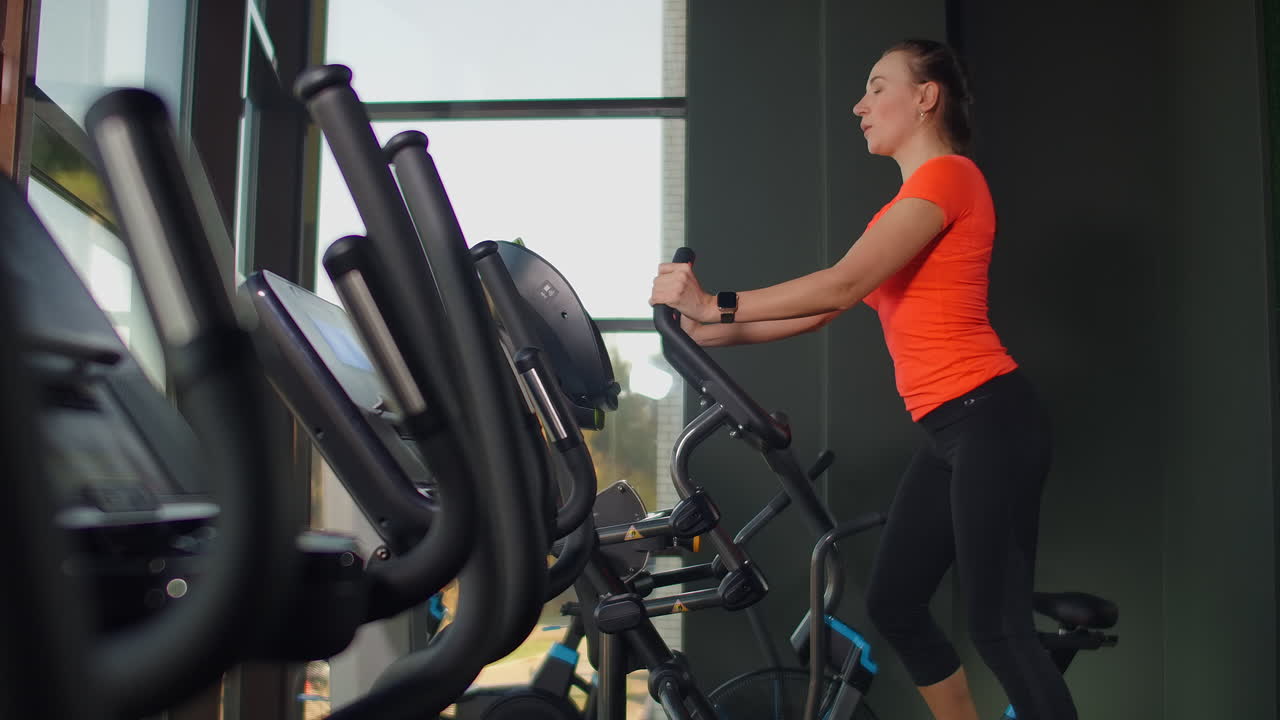 Cute young brunette doing thigh exercises on the simulator. Modern simulators near the panoramic window.