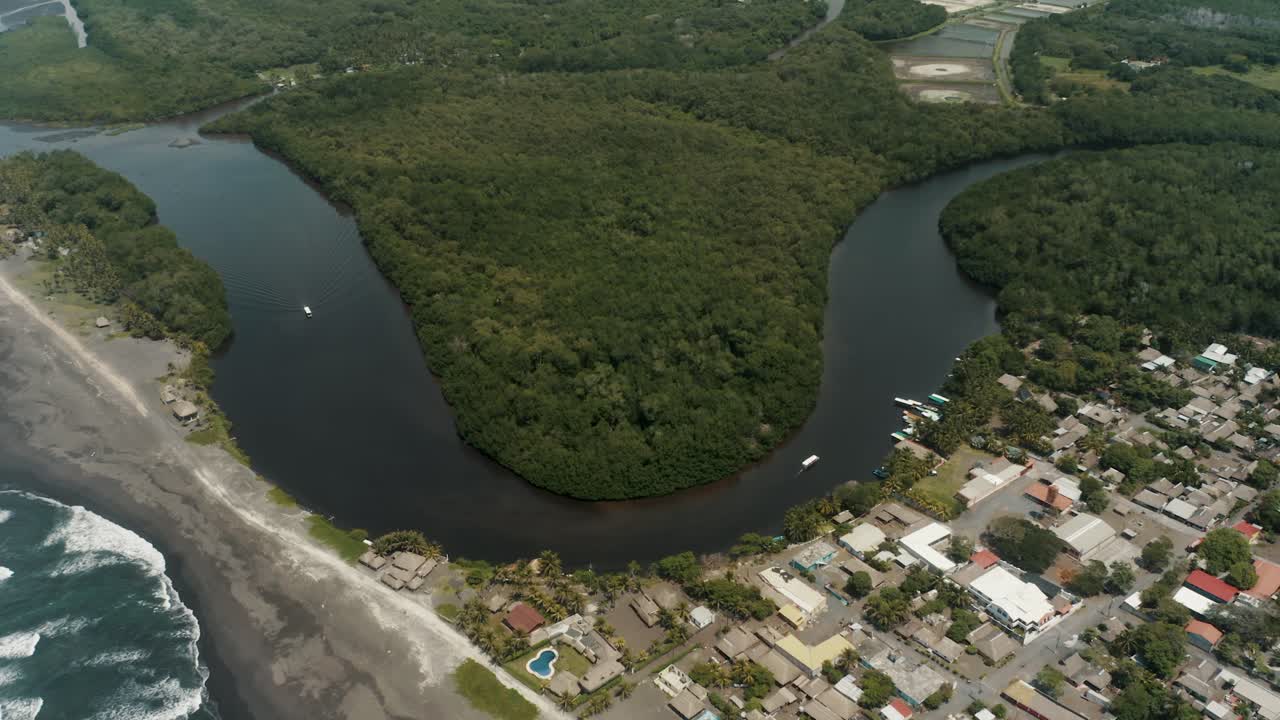 Två båtar som färdas längs floden med utsikt över en liten by omgiven av frodig grön vegetation i El Paredon, Guatemala, Centralamerika