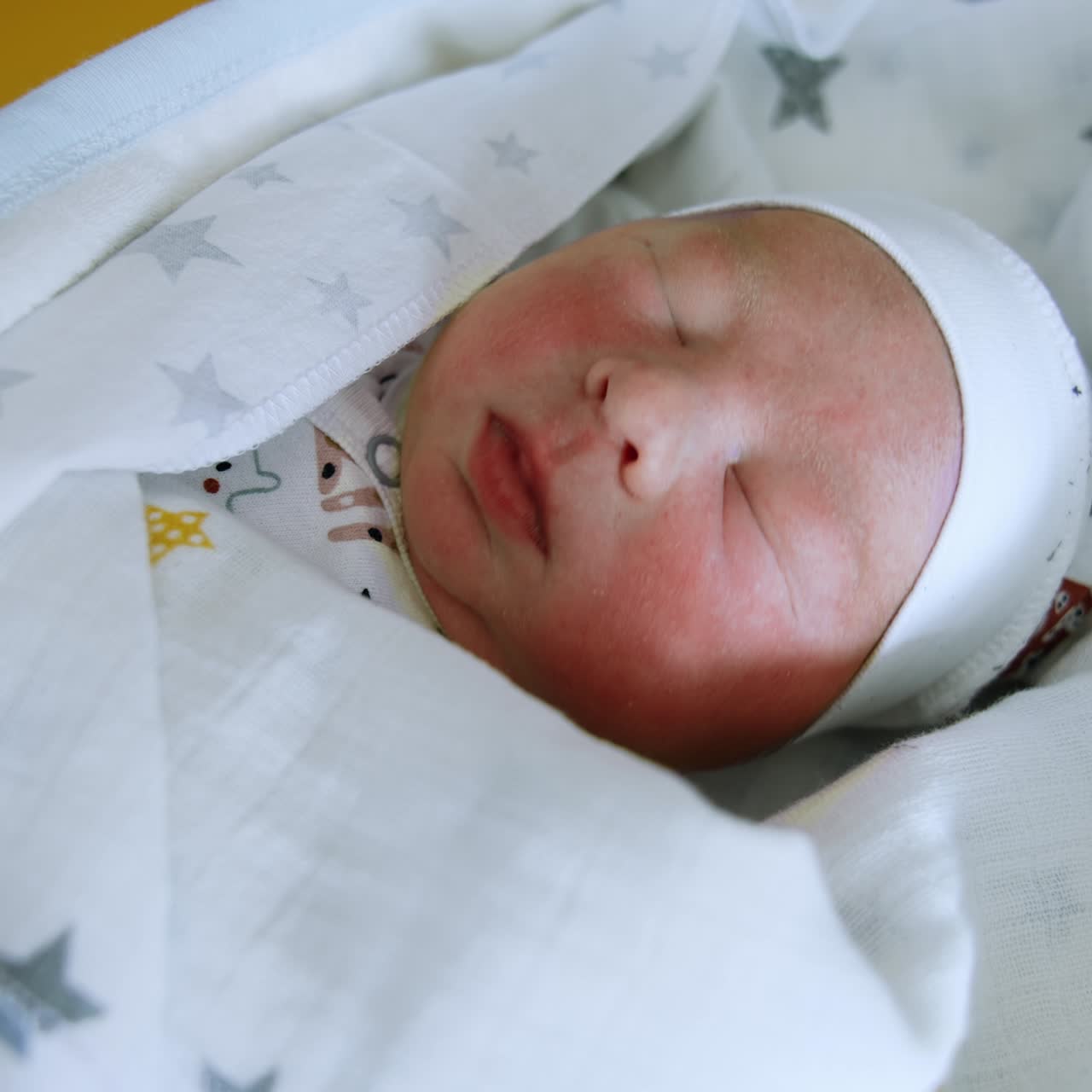 Newborn baby wearing cute cap sleeps peacefully covered in blanket. Close up. Top view