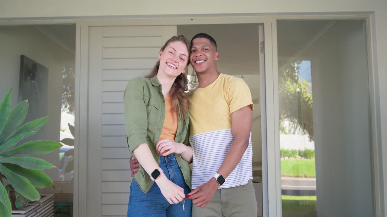 Pareja celebrando que ha recibido la llave de su casa, sosteniendo la llave hacia la cámara, abrazándose y sonriendo en la puerta