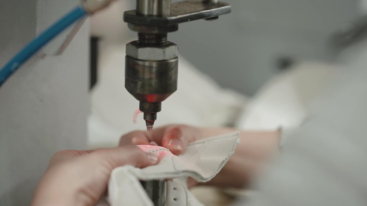 Closeup of industrial sewing machine needle stitching white leather while hands guide material during production process