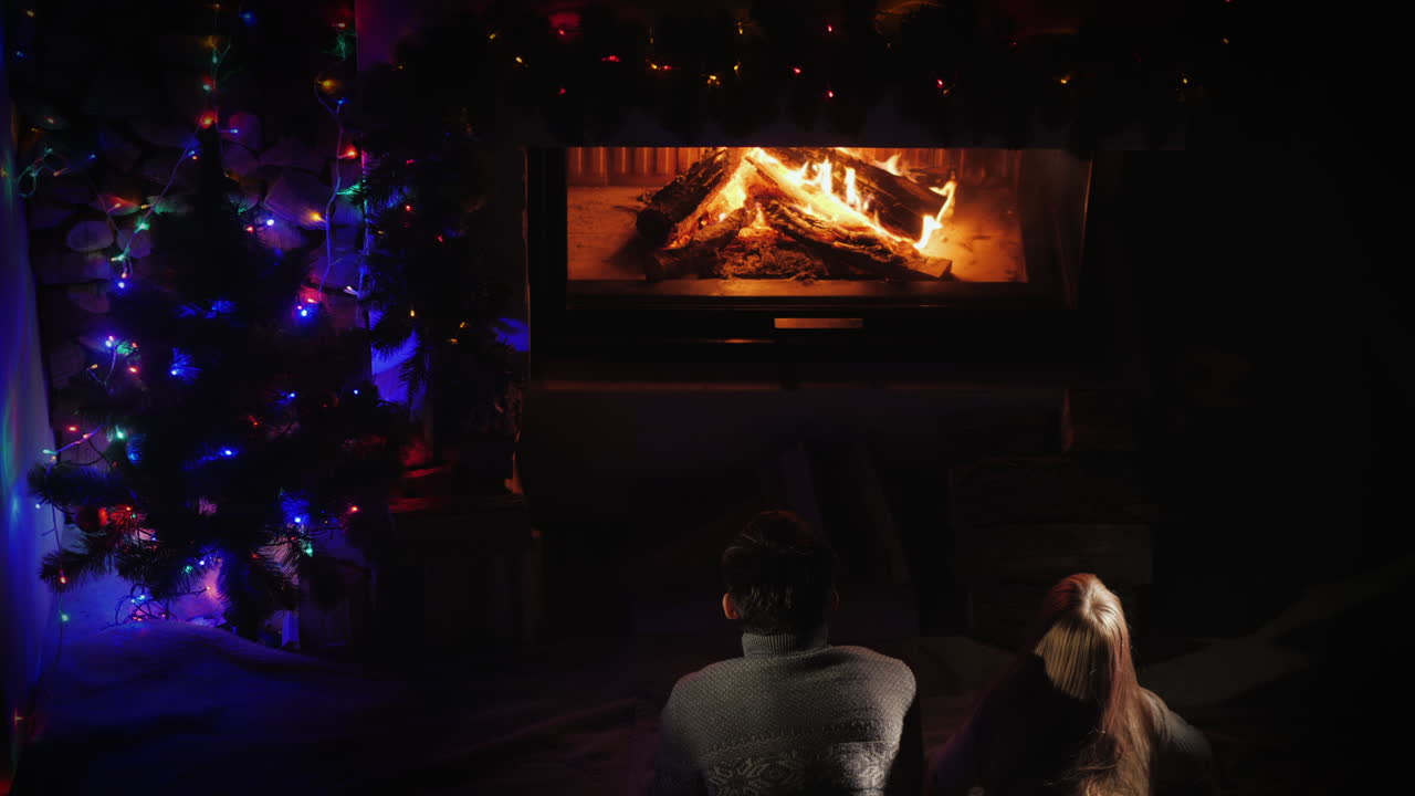 두 십대는 크리스마스 트리 근처의 벽난로에서 불을 존경합니다