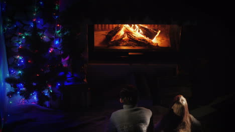 two teenagers admire the fire in the fireplace near the christmas tree