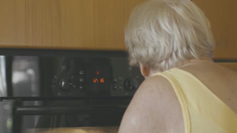 an elderly woman looks at the oven and chooses what temperature and timer to use to bake a cake