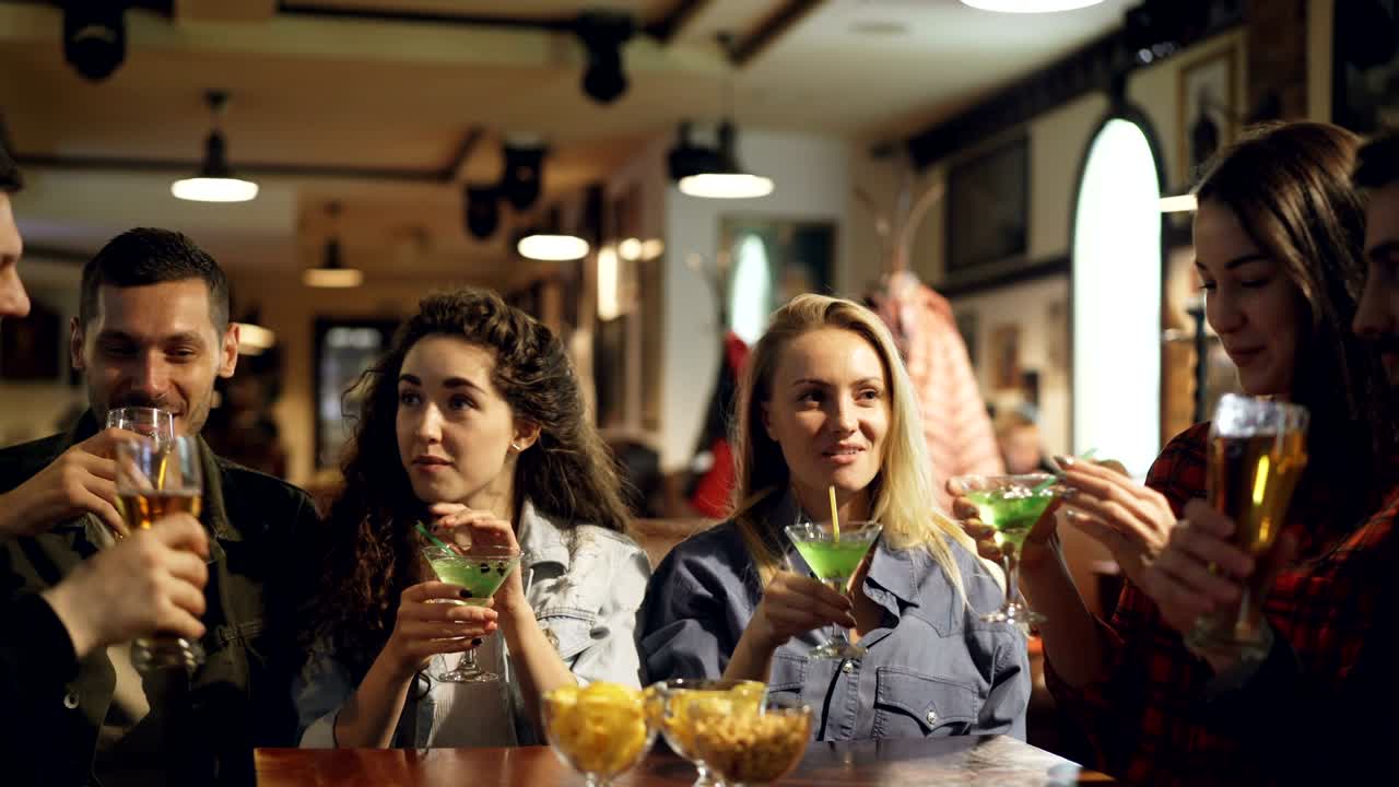 gli studenti stanno festeggiando la fine della sessione accademica in un pub moderno. stanno brindando, suonando bicchieri e bevendo bevande alcoliche. i giovani si stanno divertendo.