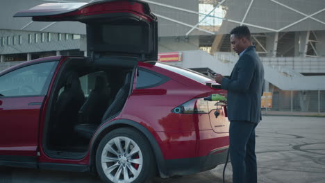 hombre de negocios cargando un coche eléctrico en el estacionamiento del estadio