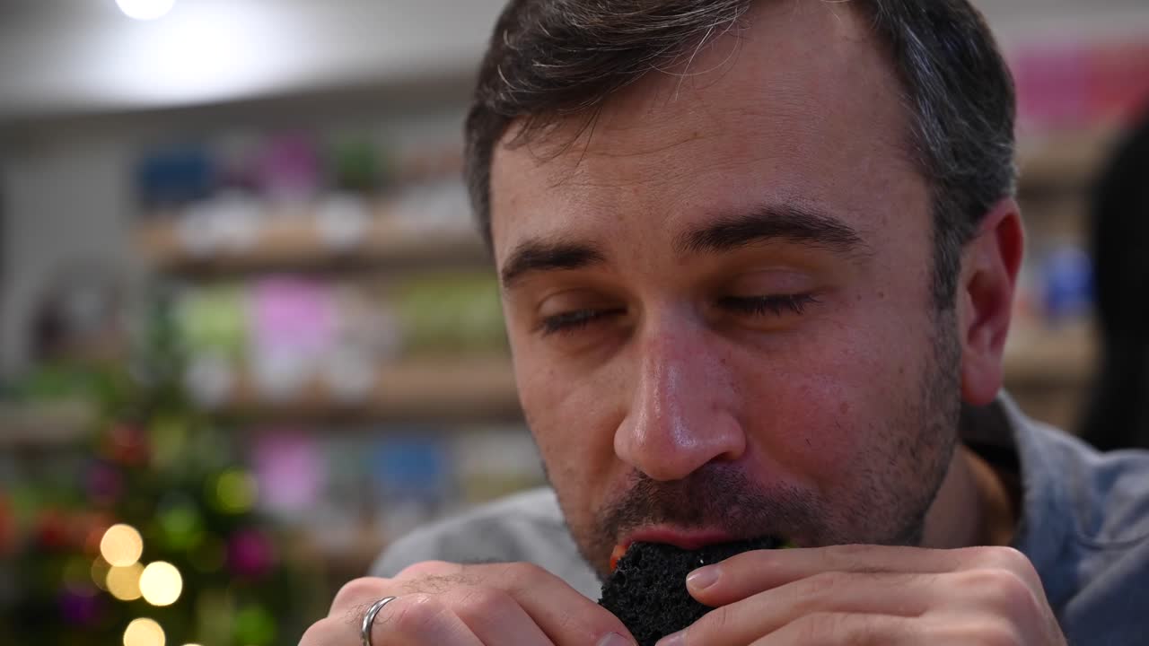 Close up of a man eating a burger with black buns