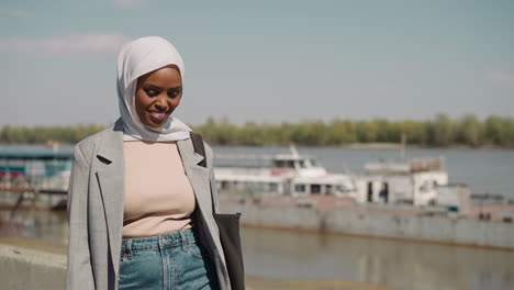 Joyful-Muslim-woman-with-headscarf-walks-along-waterfront