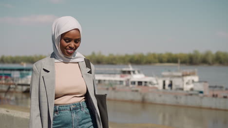 joyful muslim woman with headscarf walks along waterfront