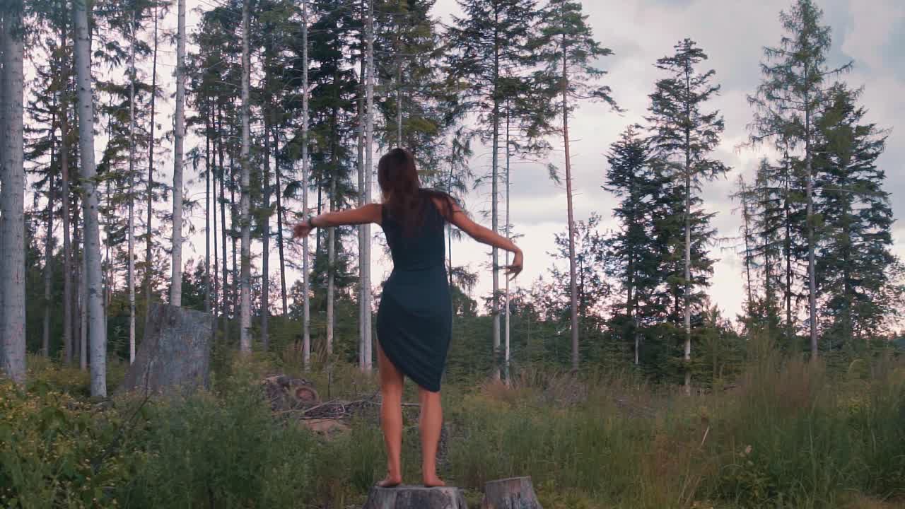 Dark Toned young beautiful Woman in Tight black Dress Dances on Tree Stump Among Nature Outdoors in the Forest, Slow Motion