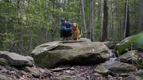 a young woman and her dog stop on large rock during hiking trail in upstate new york