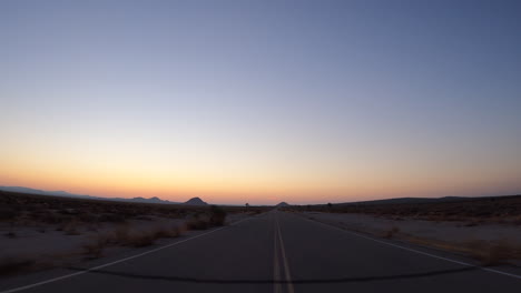 在一個孤獨的道路上穿過莫哈維沙漠的車輛在風景如畫的日落 - 觀點