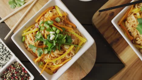 composition of bowls with pad thai, vegetables, sauces and spices on wooden background