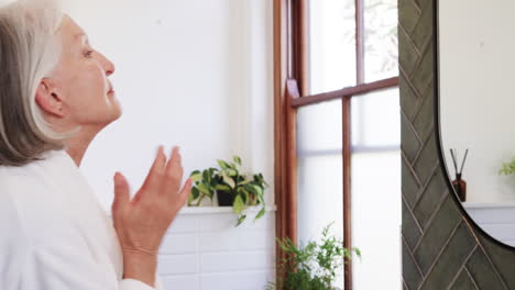 Senior woman applying skincare in bathroom, enjoying peaceful morning routine, at home