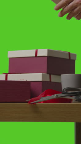 vertical video of man putting present into gift wrapped box on table shot against green screen 4