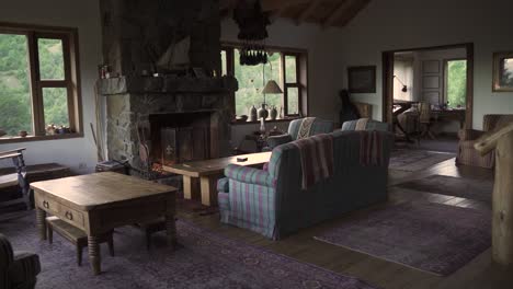 Cozy-and-elegant-large-living-room-with-sofas,-hearth,-little-table-and-nature-view-windows-in-big-wooden-house-Slow-Motion-and-60fps