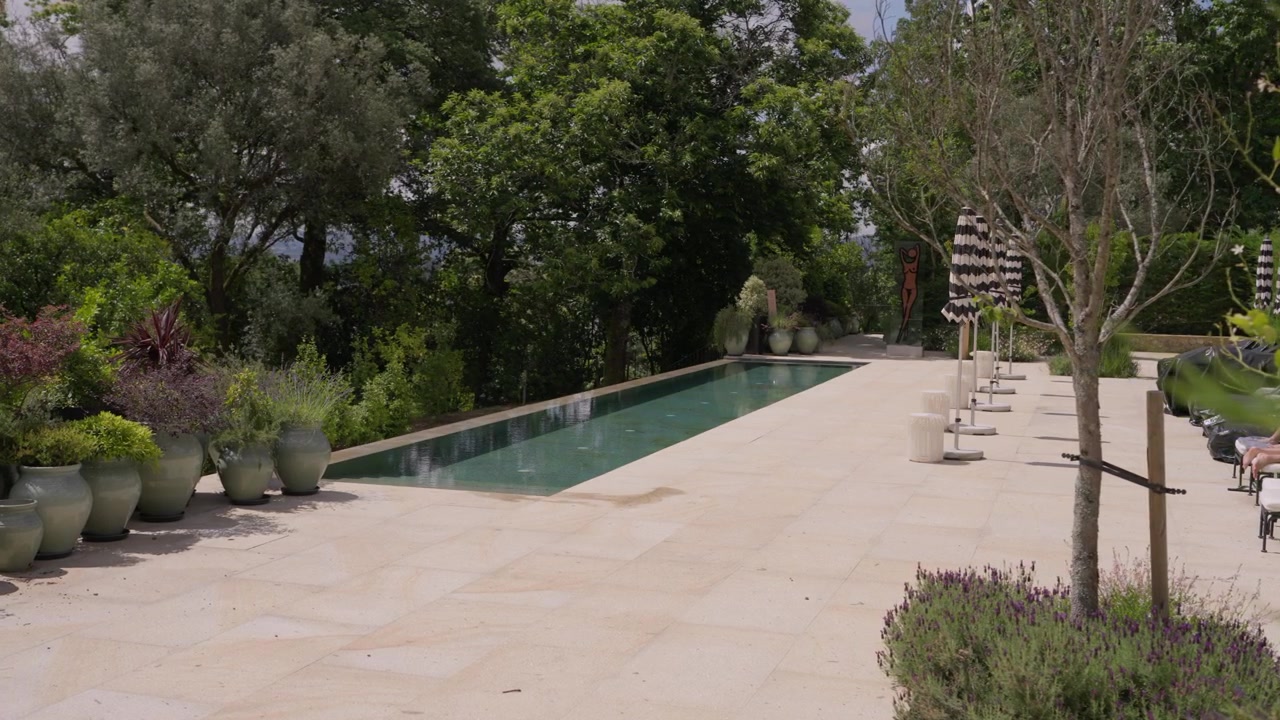 Elegante piscina rettangolare su terrazza in pietra con vasi in ceramica, alberi rigogliosi e giardino in una villa di lusso.