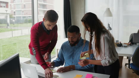 jóvenes empleados sistematizando notas adhesivas en la mesa.