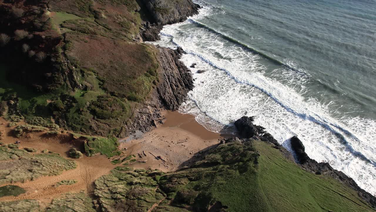 Drone rising and pulling away from Pobbles Bay with expanding views of the open sea and dramatic coastline in Wales