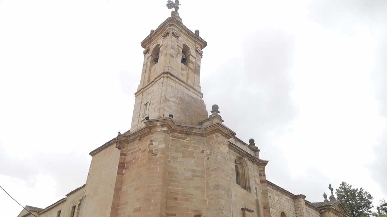Panoramica verso l'alto di una storica chiesa in pietra e del campanile sotto un cielo nuvoloso drammatico in Spagna