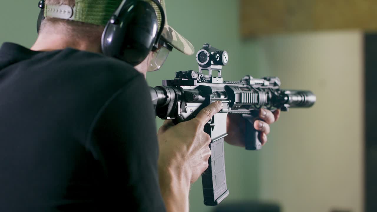 vista trasera de un hombre con protección para el oído disparando un rifle en un campo de tiro interior