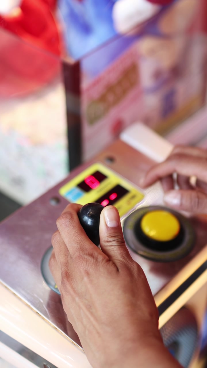 Primo piano di mani che giocano a una macchina arcade con artiglio