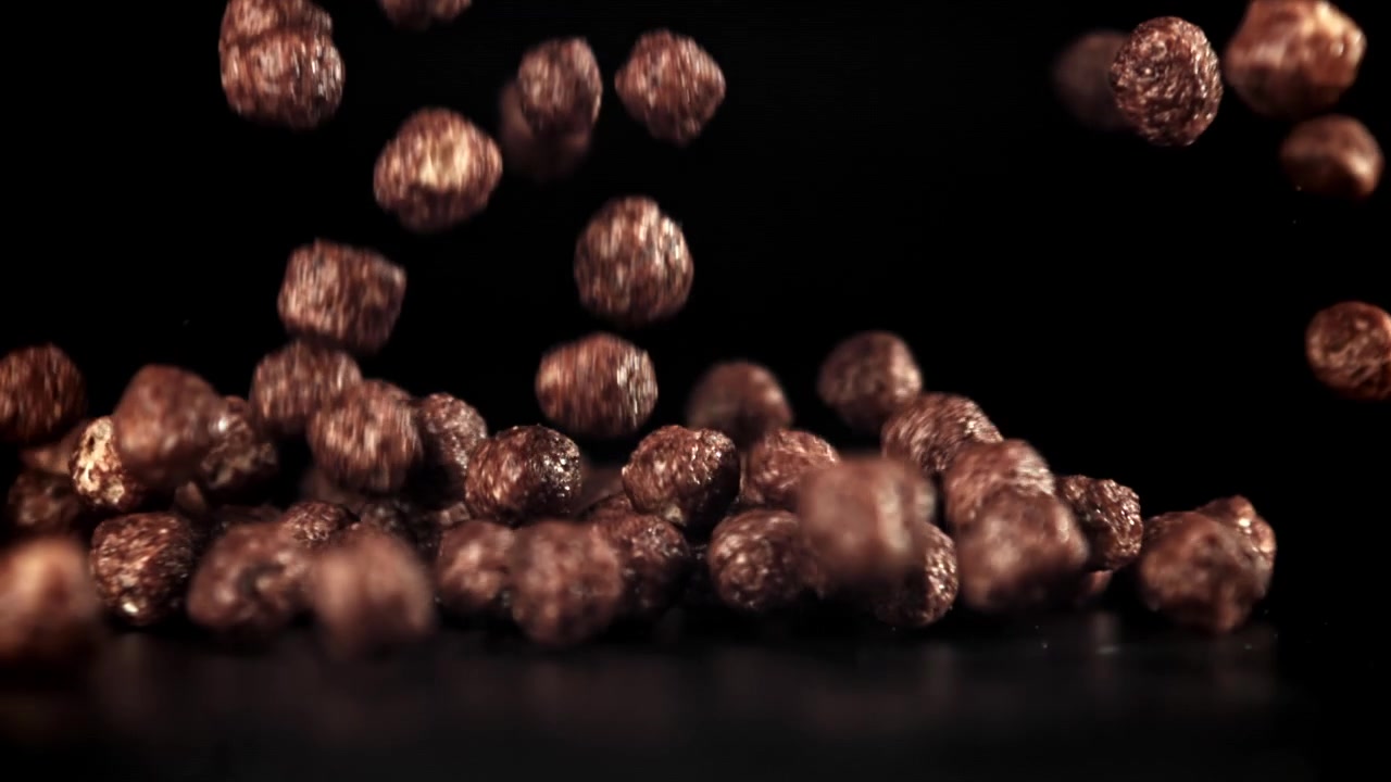 Zeitlupe von Schoko-Müsli-Kugeln, die auf eine schwarze Oberfläche fallen