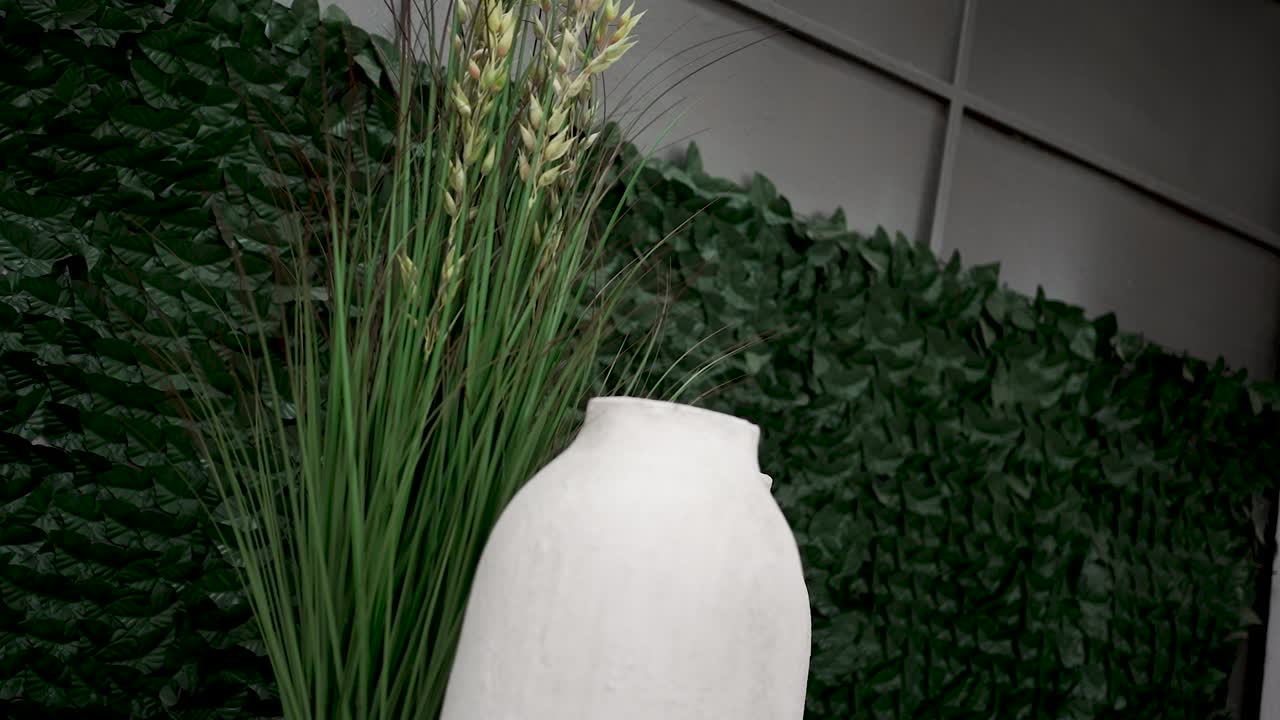 A stylish ceramic vase stands elegantly, filled with tall grasses, set against a lush green backdrop. This modern décor enhances the room's aesthetic appeal and atmosphere