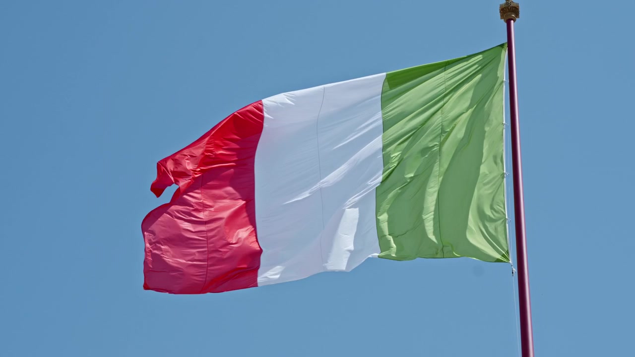 Bandiera nazionale italiana che sventola su un'alta asta contro un cielo azzurro brillante, utile per temi di politica, cultura o viaggi