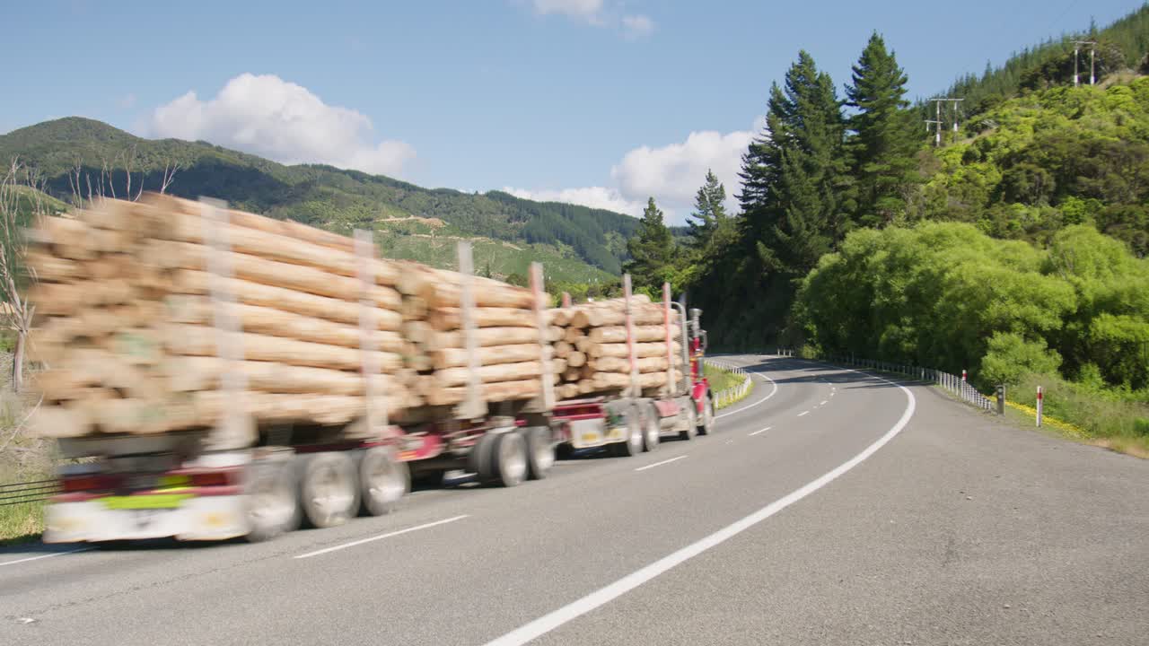 Cars and a logging truck driving past the camera and around a corner on a road in rural New Zealand
