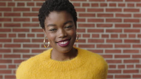 Retrato-De-Una-Mujer-Afroamericana-Segura-De-Sí-Misma-Sonriendo-Alegremente-Usando-Una-Camiseta-Amarilla-Sobre-Fondo-De-Pared-De-Ladrillo